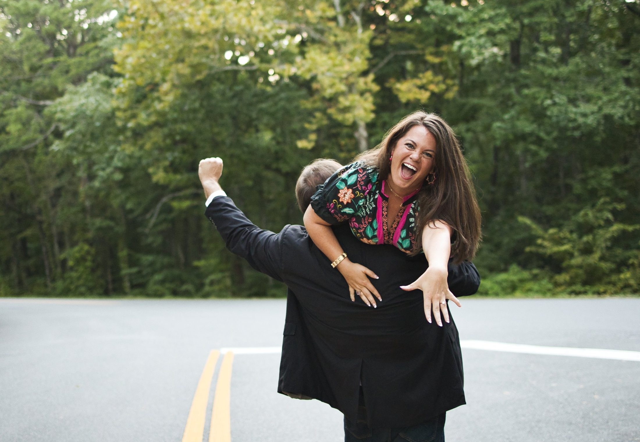 Celebrating on a tree-lined road, one arm raised in victory, ring hand out toward the camera